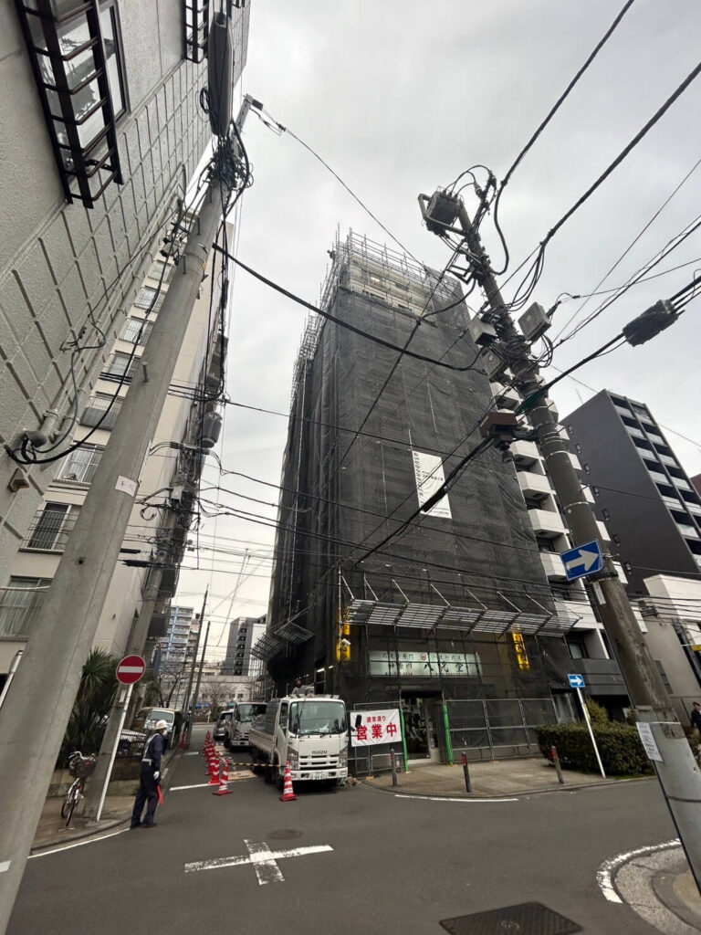 工事中のビルが黒いシートで覆われ、作業車が駐車されている都市の一角